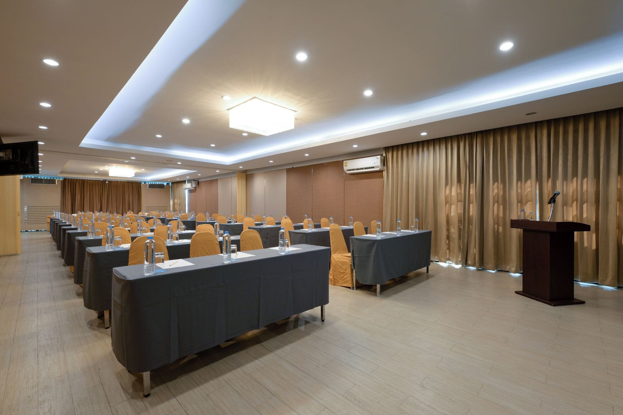 Een congreszaal met rijen tafels, een spreekgestoelte en een airconditioning.