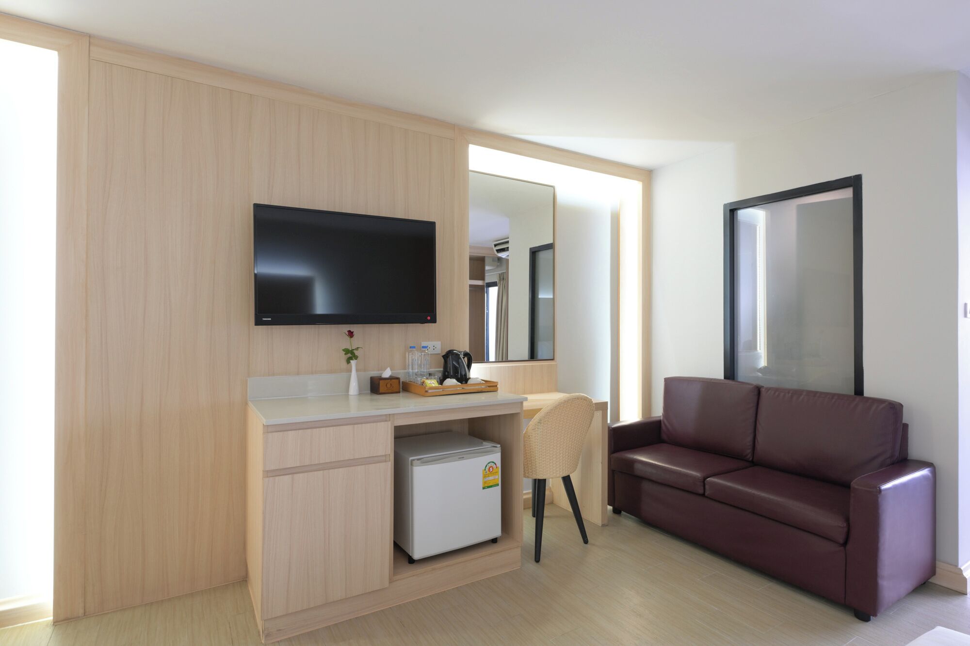 Una habitación de hotel moderna con televisión de pantalla plana, un refrigerador pequeño, un sofá y un espejo.