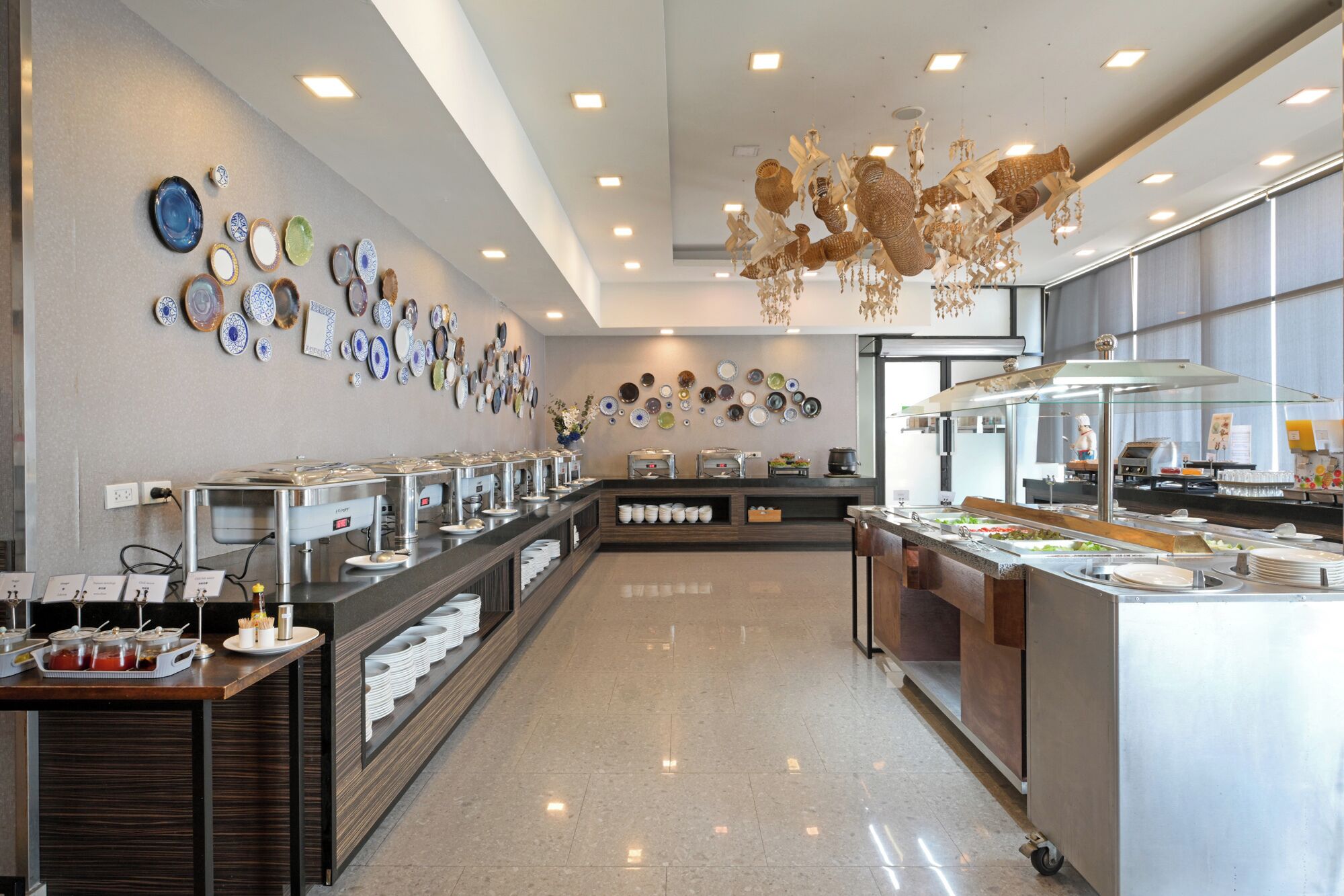 A buffet area with multiple serving stations, a wall decorated with various plates, and a modern chandelier.