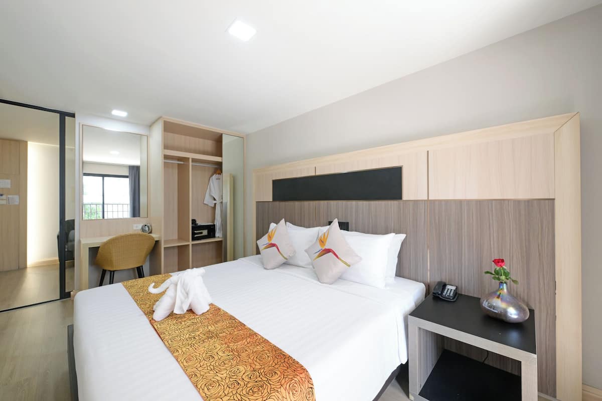 A hotel room with a bed, bedside table, a mirror, a wardrobe, and a desk.