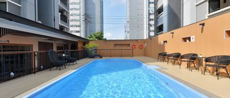 A swimming pool with lounge chairs and tables, surrounded by apartment buildings.