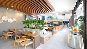 A modern hotel lobby with a seating area, a bar, and a large screen displaying a presentation.