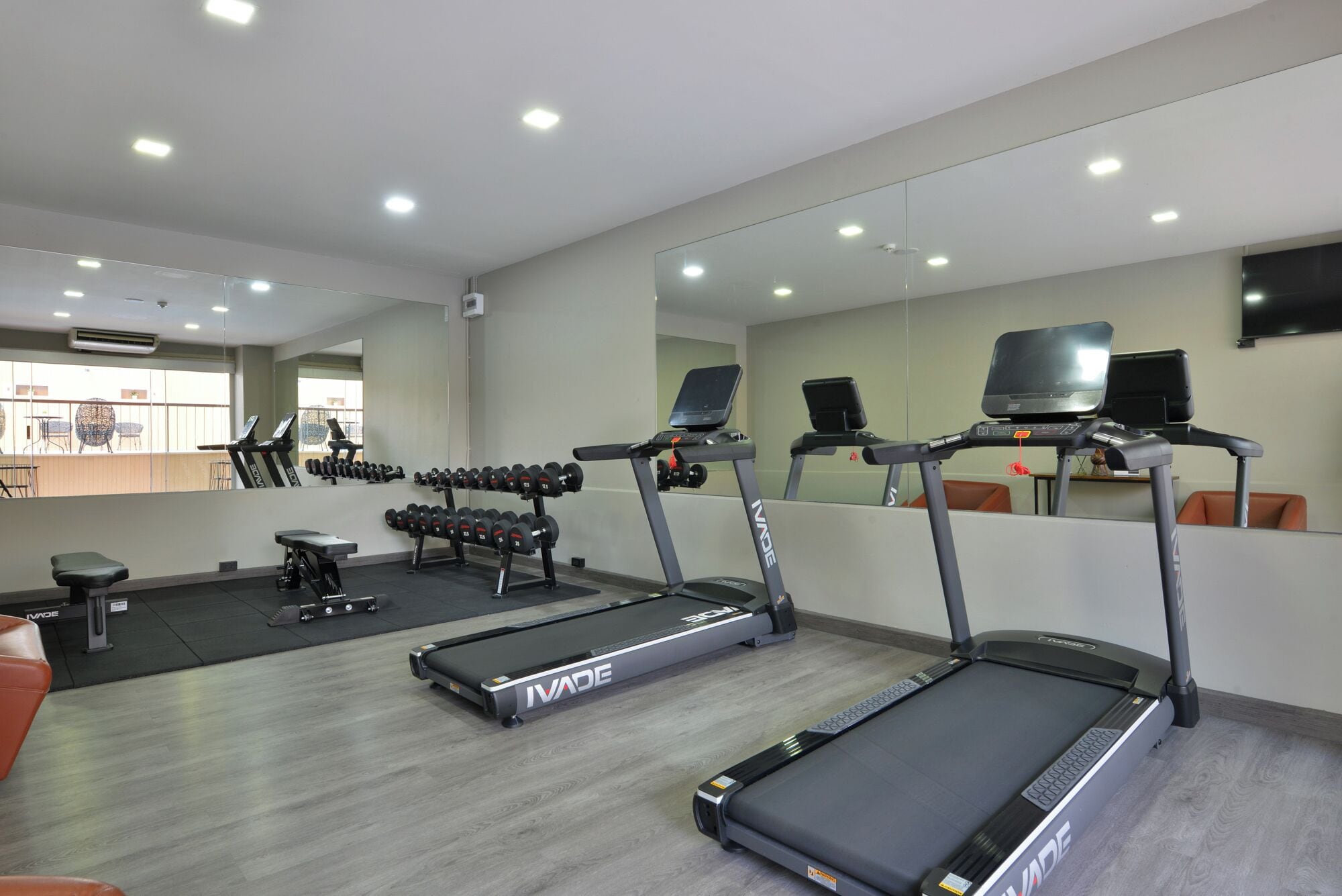 Une salle de sport équipée de tapis de course, d’haltères et d’un mur recouvert de miroirs.