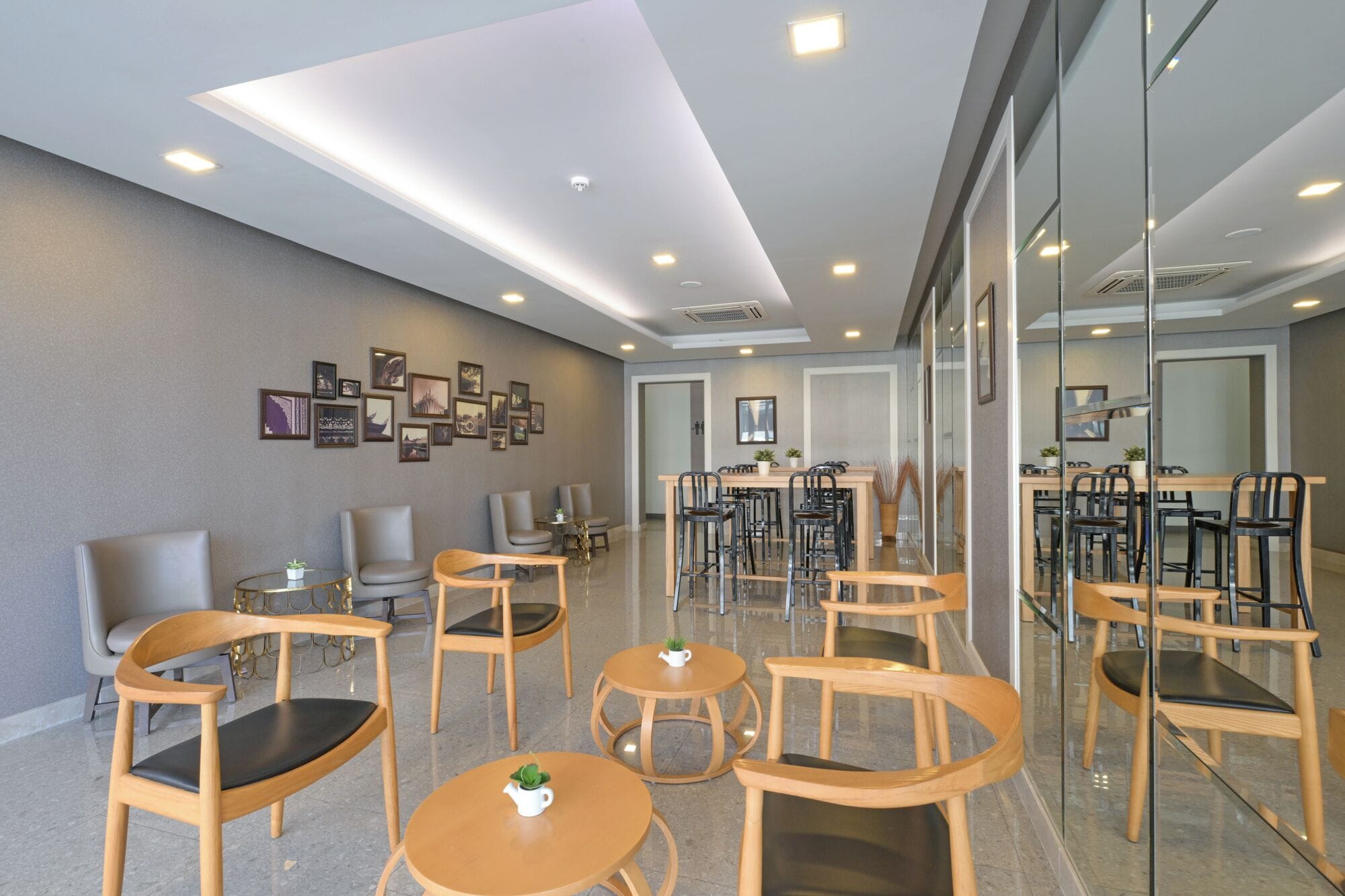 A modern hotel lobby with a glass partition, multiple seating areas, and a wall adorned with framed pictures.