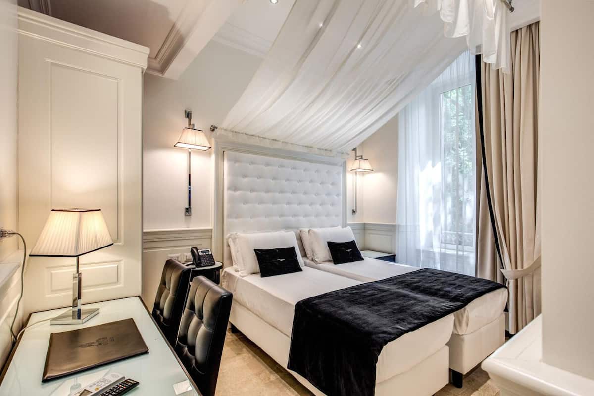 A hotel room with a large bed, two bedside tables, a desk with a lamp, and a chair.
