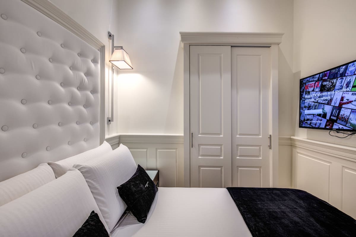 A hotel room with a tufted headboard, a flat-screen TV mounted on the wall, and a closed door.