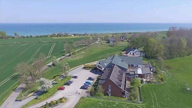 Una casa grande con entrada para coches y aparcamiento, rodeada de campos verdes y vistas al mar.