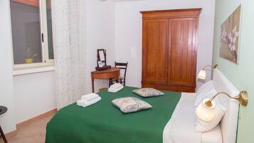 Un dormitorio ordenado con colcha verde, un armario de madera, un escritorio con silla y una lámpara de noche.