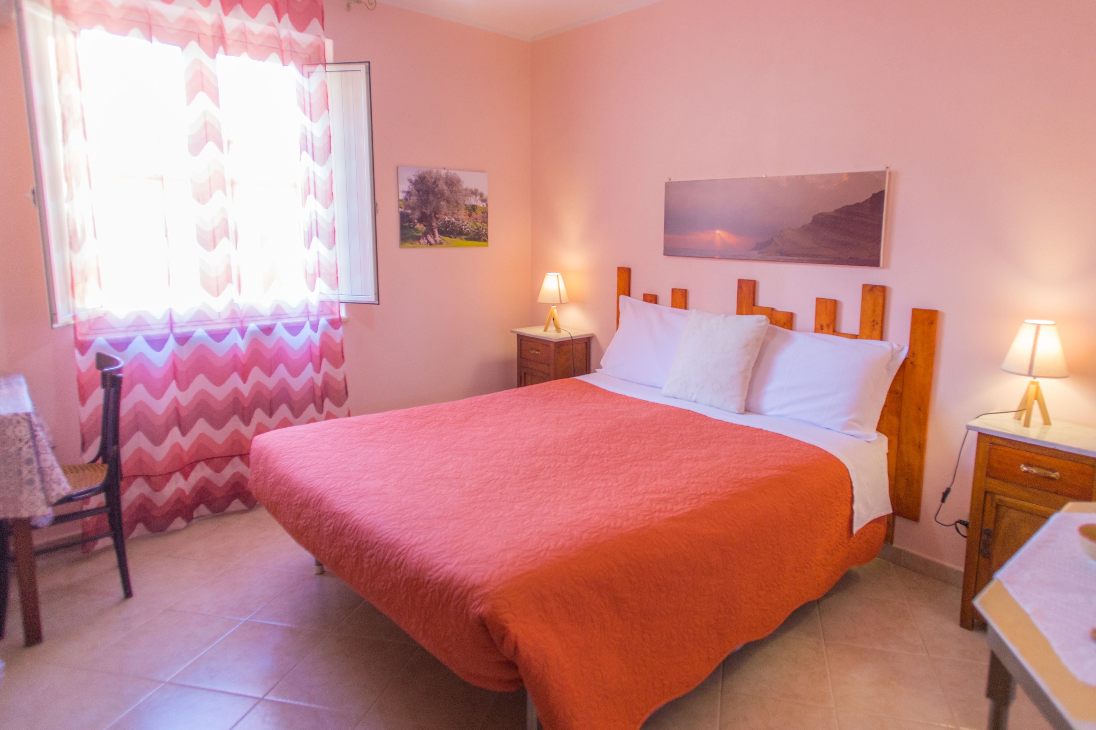 A bedroom with a large bed, two bedside tables with lamps, a chair, a table, and a window with curtains.