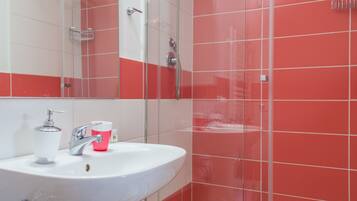 A bathroom with a white sink, a glass shower enclosure, and red-tiled walls.
