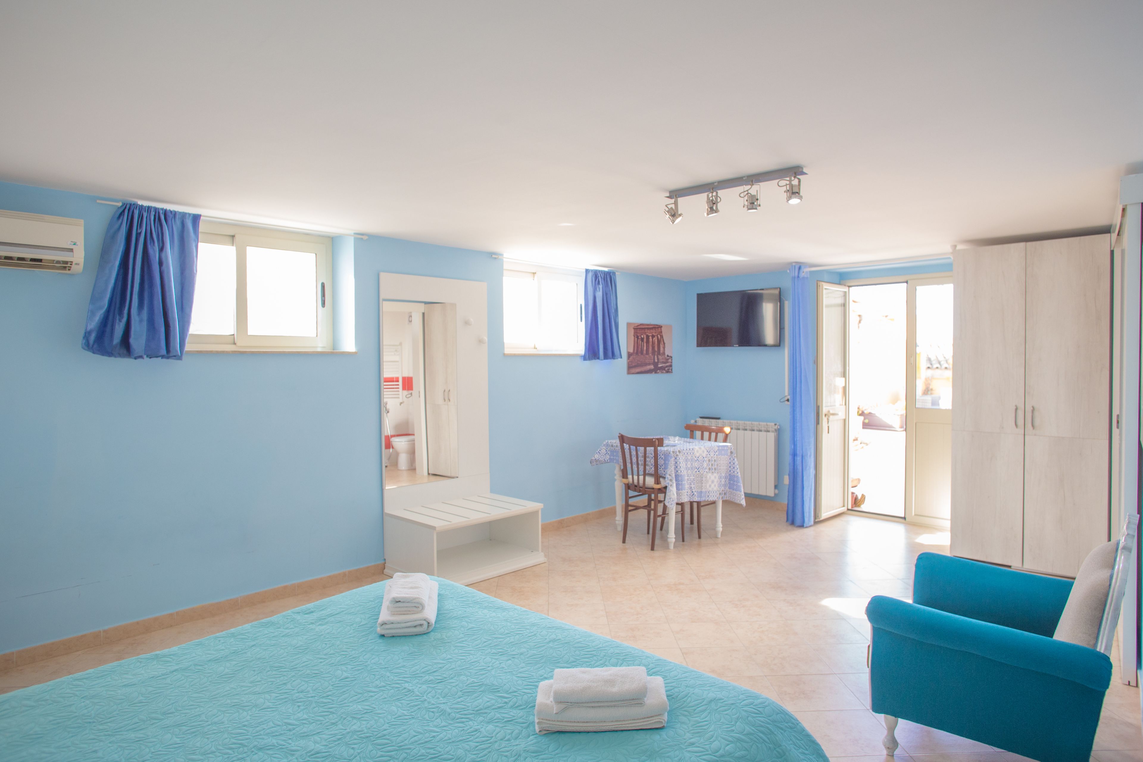 Una habitación con cama, una silla azul, una mesa y un armario.