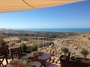 A terrace with a table set for dining, overlooking a coastal landscape with terracotta rooftops and a clear view of the sea. - Le Terrazze di Pirandello (Agrigento)