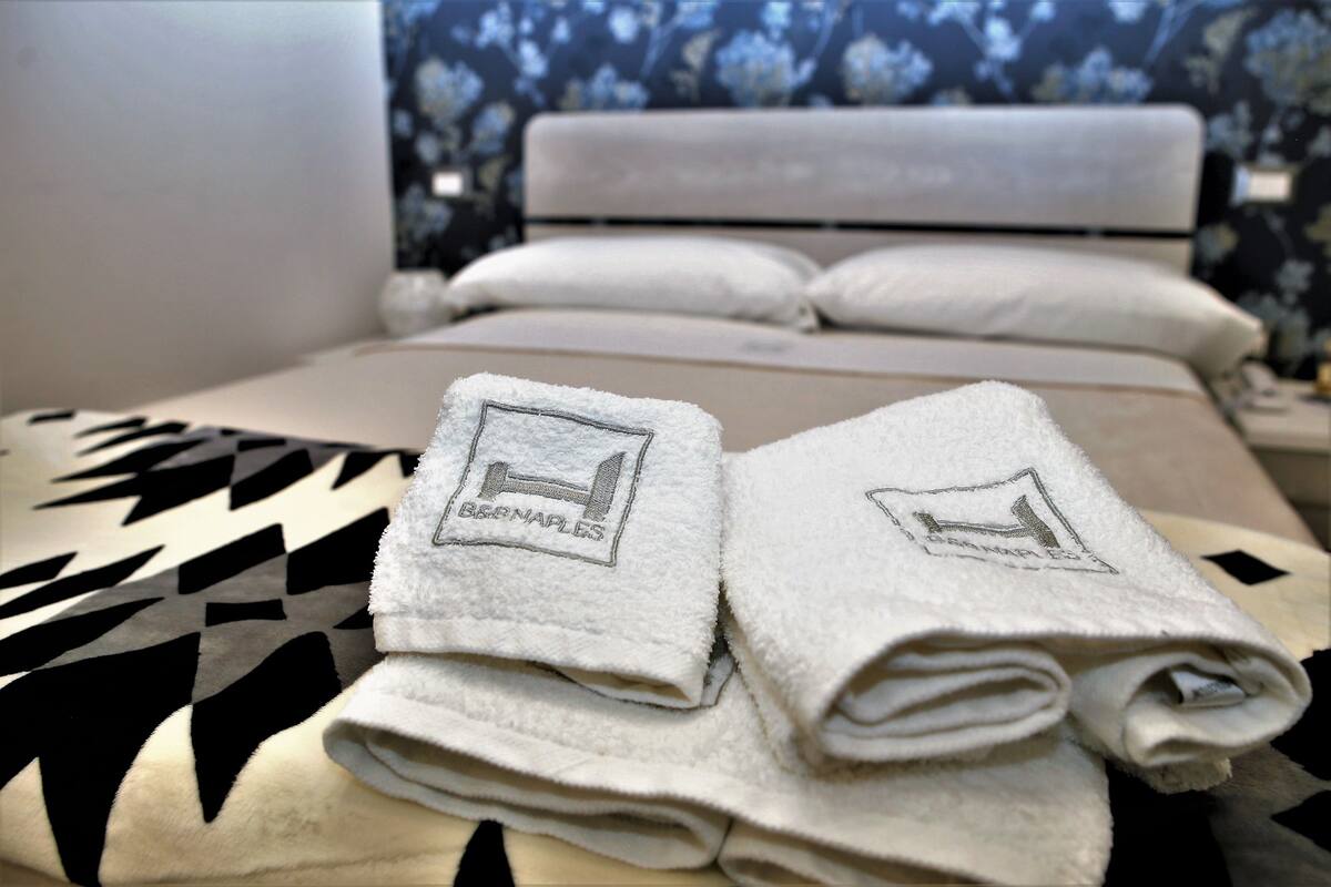 A neatly made bed with a patterned bedspread and two folded towels with a logo on them.