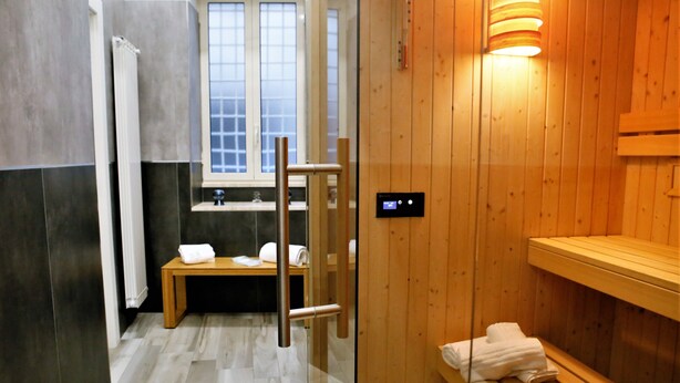 A modern bathroom with a wooden sauna, a glass shower enclosure, and a window with a view. - Hermes Rooms for tourists (Naples)