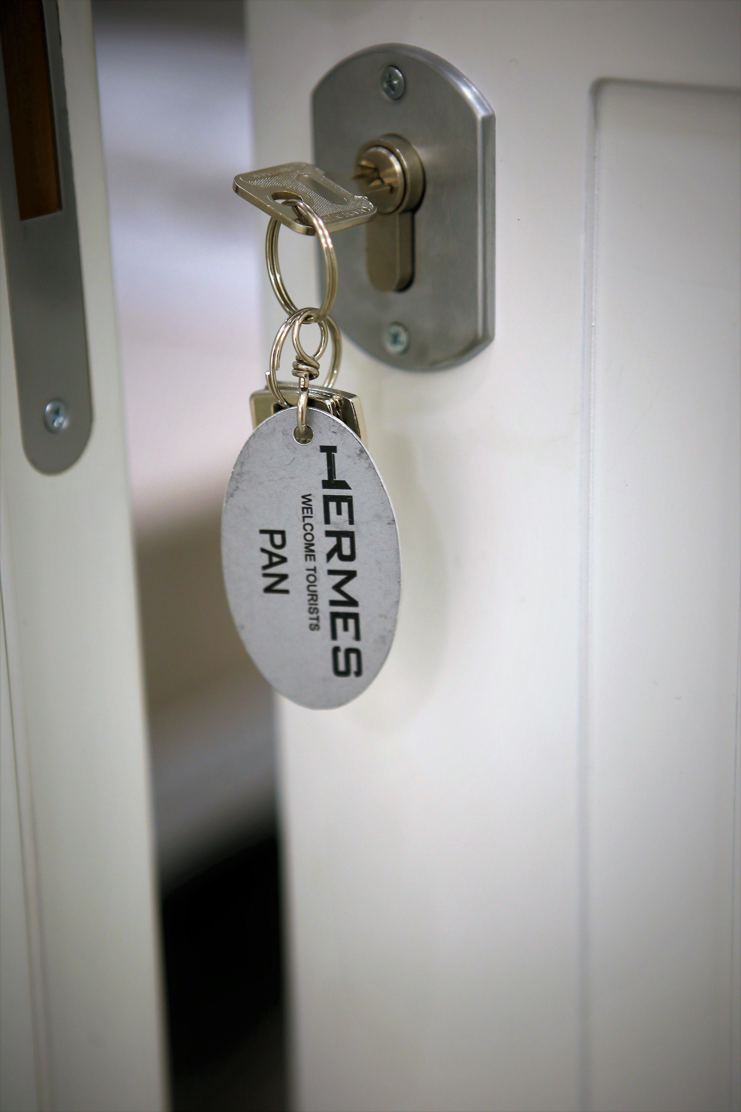 A door with a keyhole and a keychain with a metal plate that reads "HERMES WELCOME TOURISTS PAN".