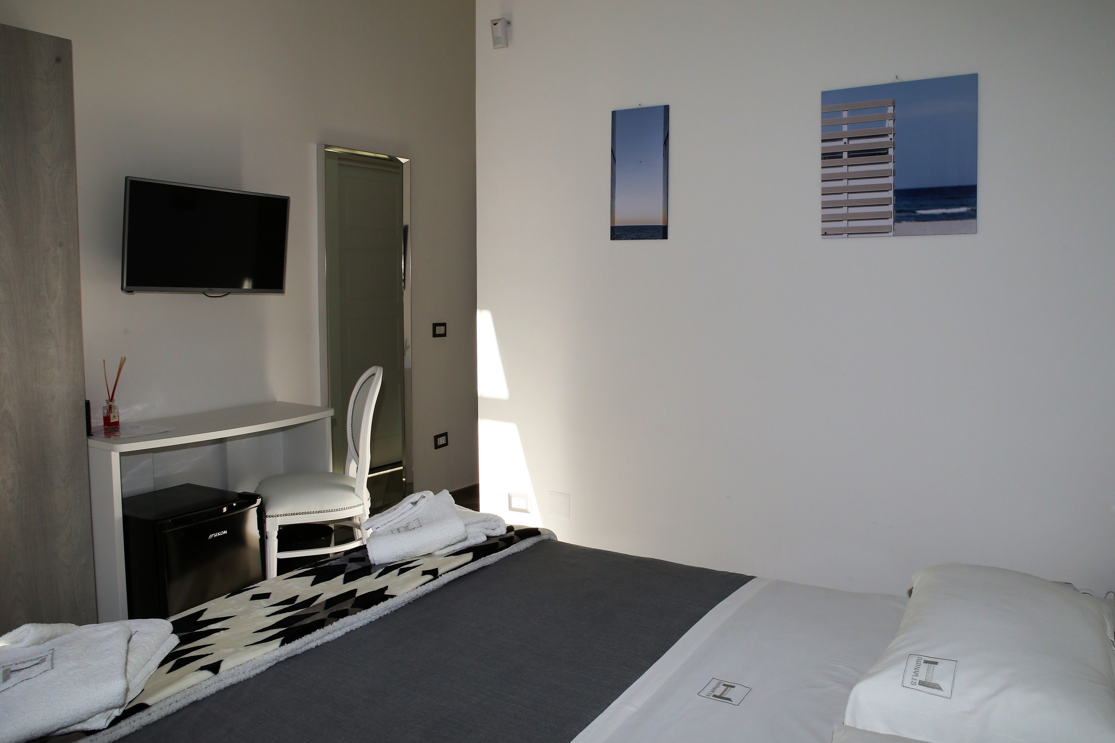A hotel room with a bed, a desk, a chair, a TV, and a window with a view of the sea.