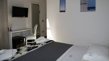 A hotel room with a bed, a desk, a chair, a TV, and a window with a view of the sea.