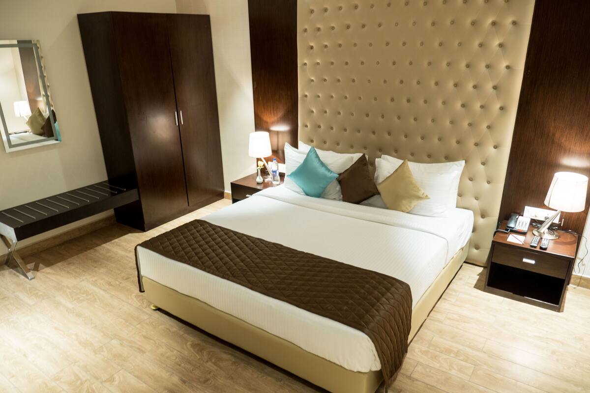 Habitación de hotel con una cama grande, un armario, una mesita de noche con lámpara y un espejo en la pared.