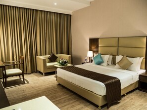 A hotel room with a large bed, a chair, a small table with a flower arrangement, and a lamp. - Hotel Grand Ashok, A Bergamont Hotel - Tanjore (Thanjavur)