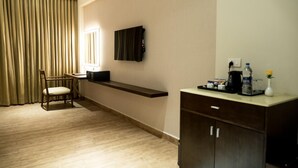 Habitación de hotel con piso de madera, un escritorio con silla, televisor de pantalla plana en la pared, minibar y una pequeña mesa con un florero.