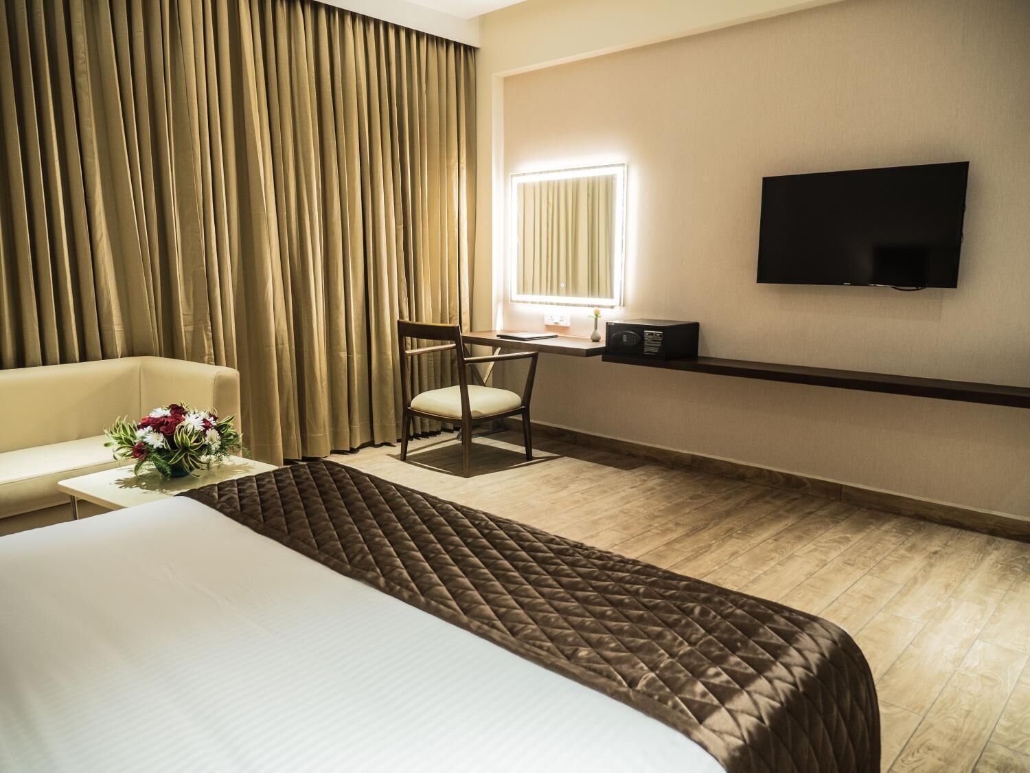 A hotel room with a large bed, a desk with a chair, a flat-screen TV, and a window with curtains.