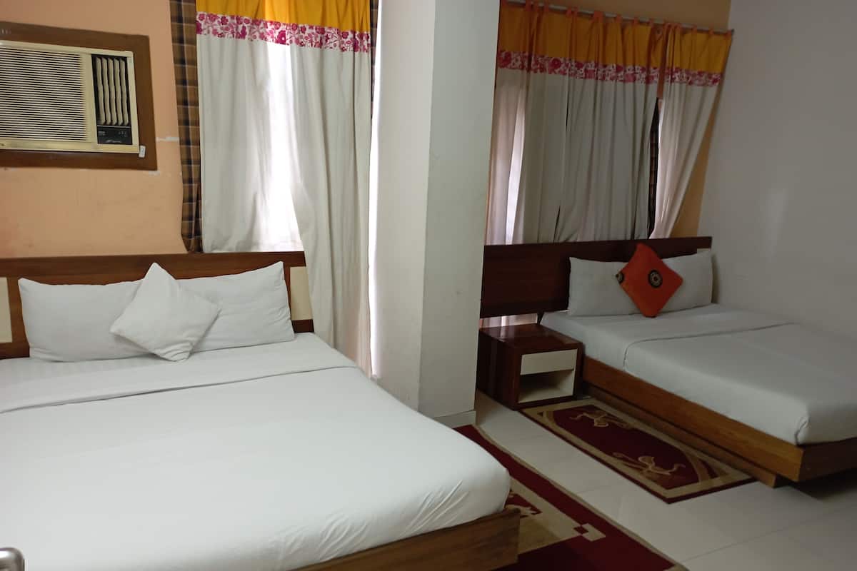 A hotel room with two beds, a nightstand, a red and white patterned rug, and a wall-mounted air conditioning unit.
