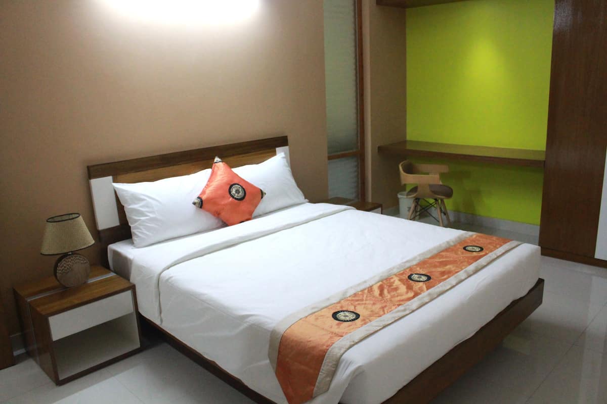 A neatly made bed with a white and orange bedspread, a wooden headboard, and a nightstand with a lamp.
