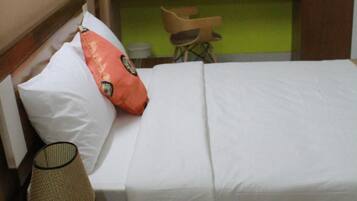 Una cama bien hecha con ropa blanca, cabecera de madera y una única almohada naranja.