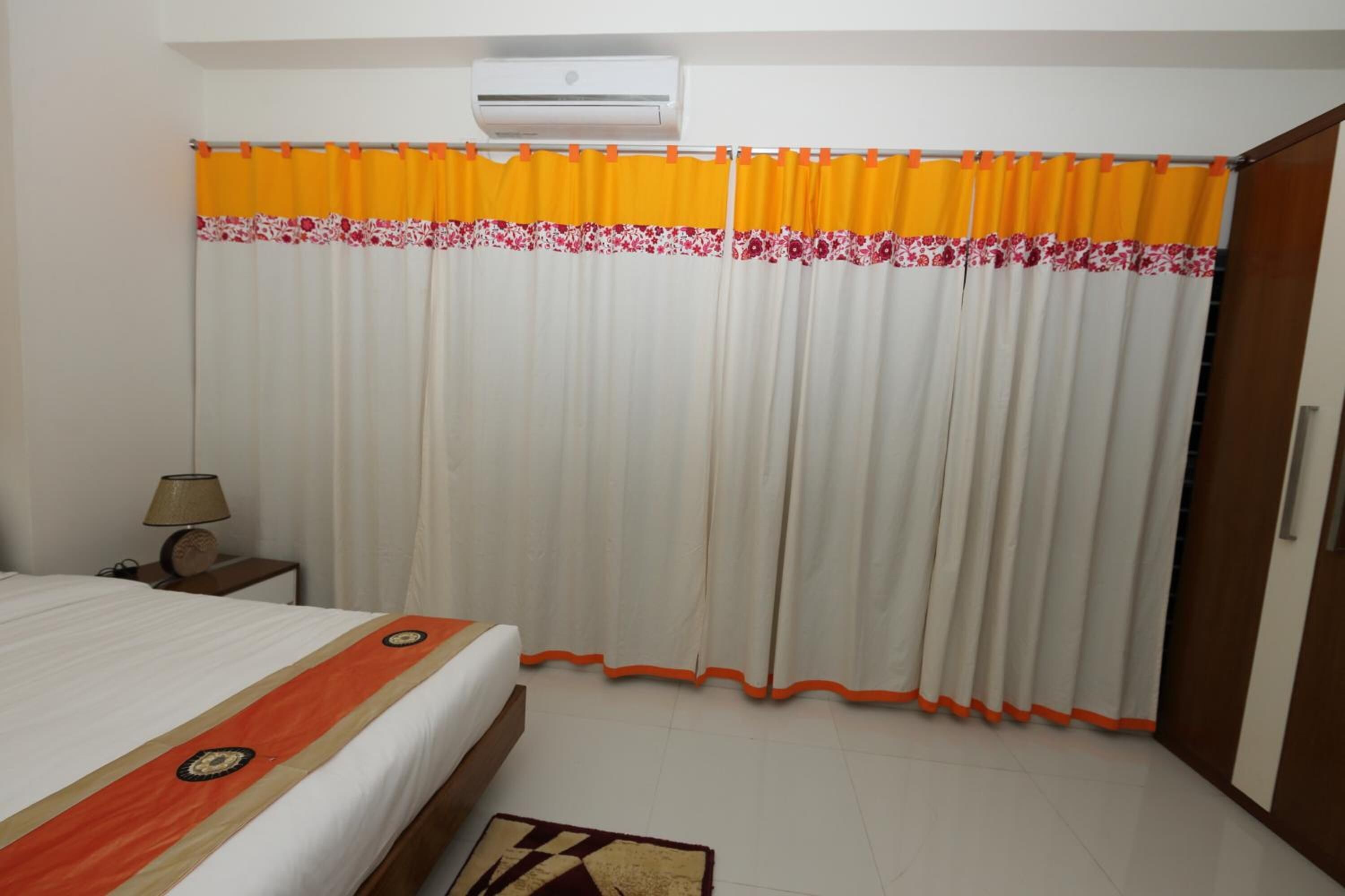 Habitació d'hotel amb un llit, aire condicionat, una taula de nit amb una làmpada i cortines amb un dibuix floral.