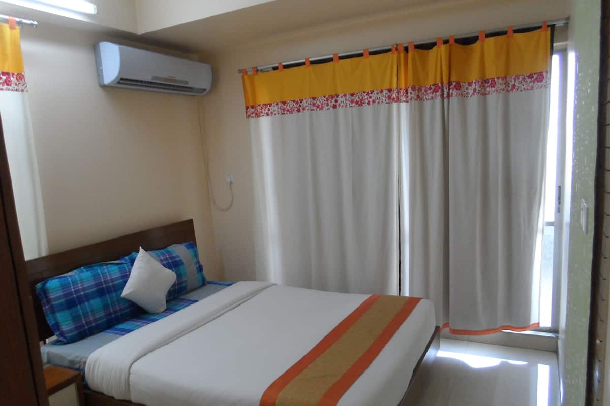 A bedroom with a bed, a nightstand, an air conditioning unit, and a window with curtains.