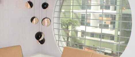 A modern living room with a beige sofa, a coffee table, and a round window with a view of buildings.