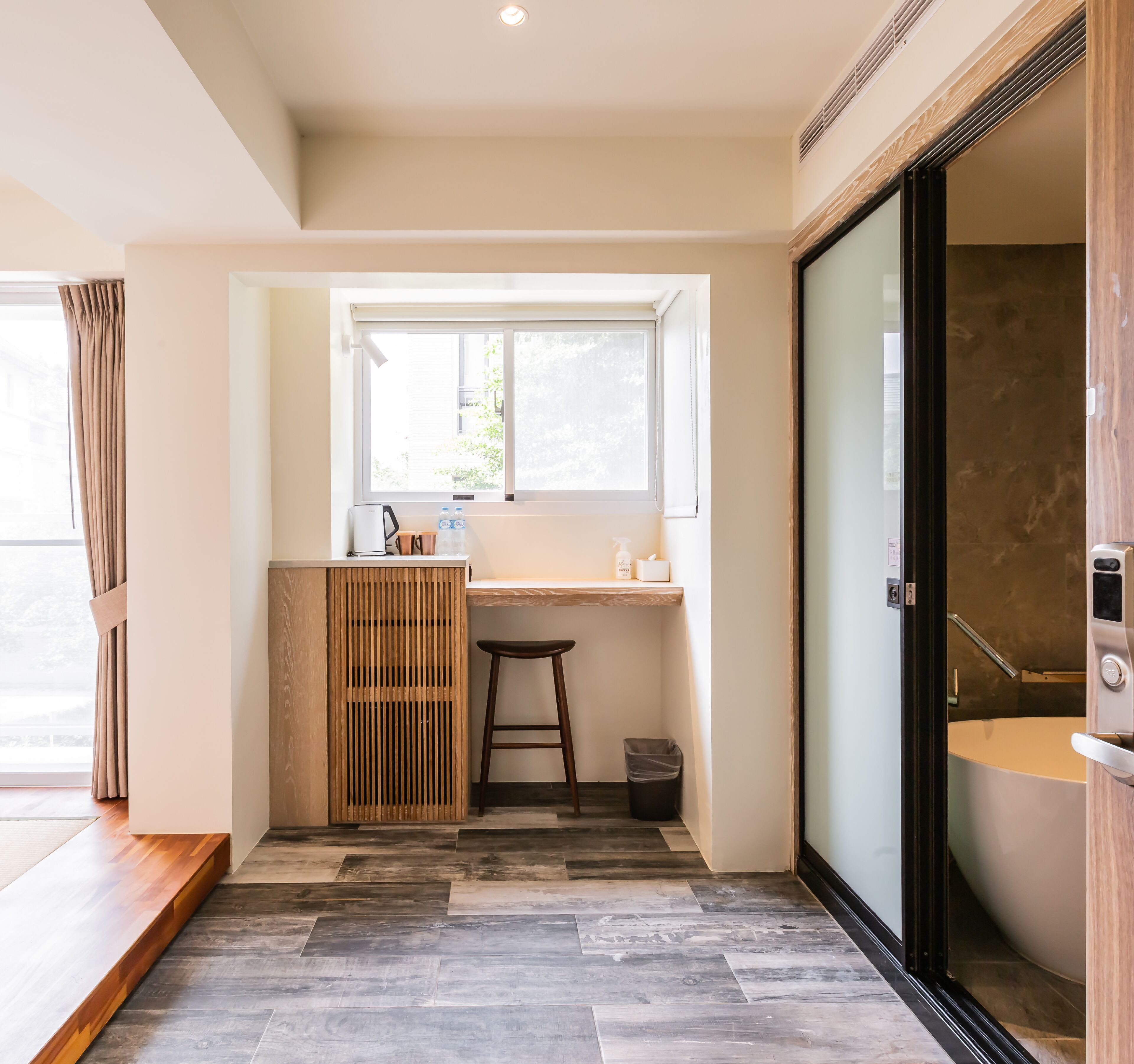 A modern bathroom with a large bathtub, a wooden vanity, a window with curtains, and a tiled floor.