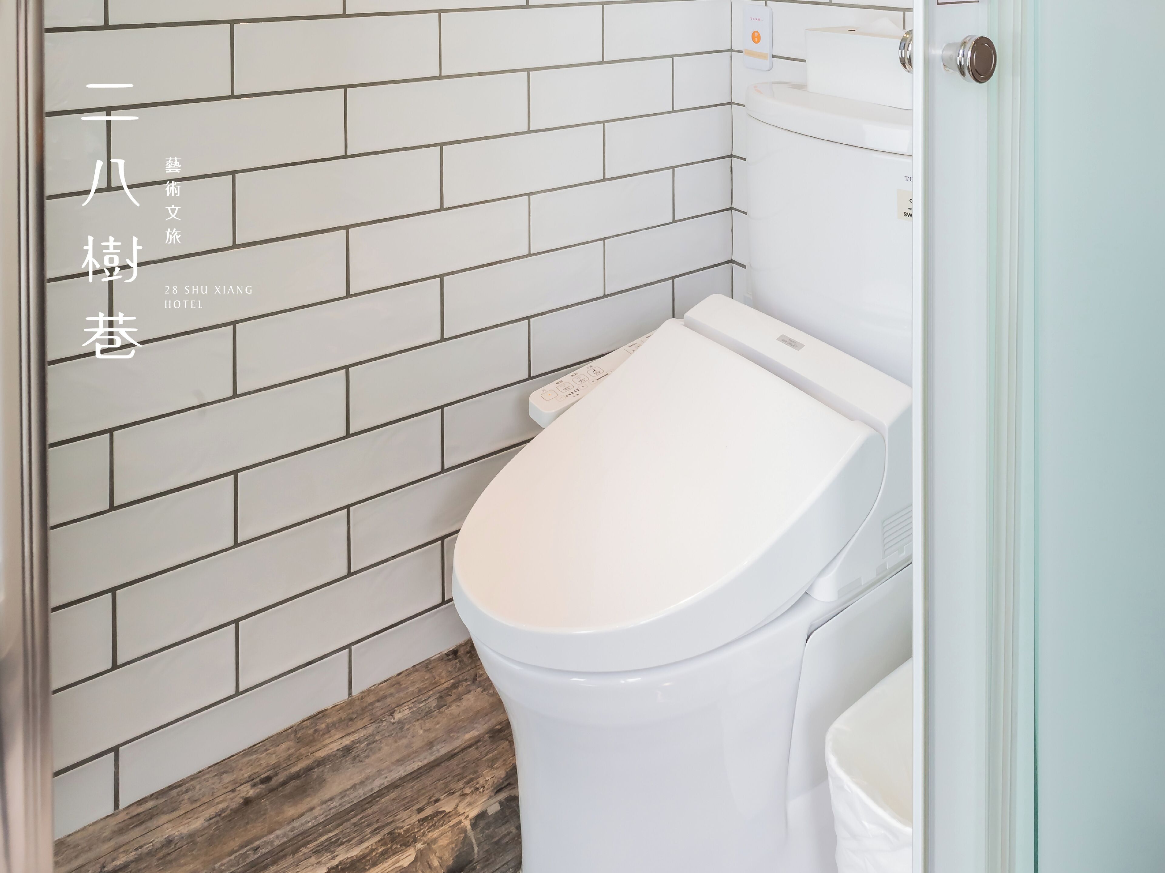 A bathroom with a white toilet, a wooden floor, and a white tiled wall.