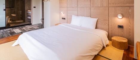 A modern hotel room with a large bed, a wooden headboard, bedside lamps, and a small wooden stool.