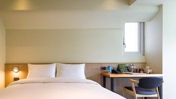 Ein Hotelzimmer mit Bett, Schreibtisch mit Stuhl, Fenster und Nachttisch mit Lampe.