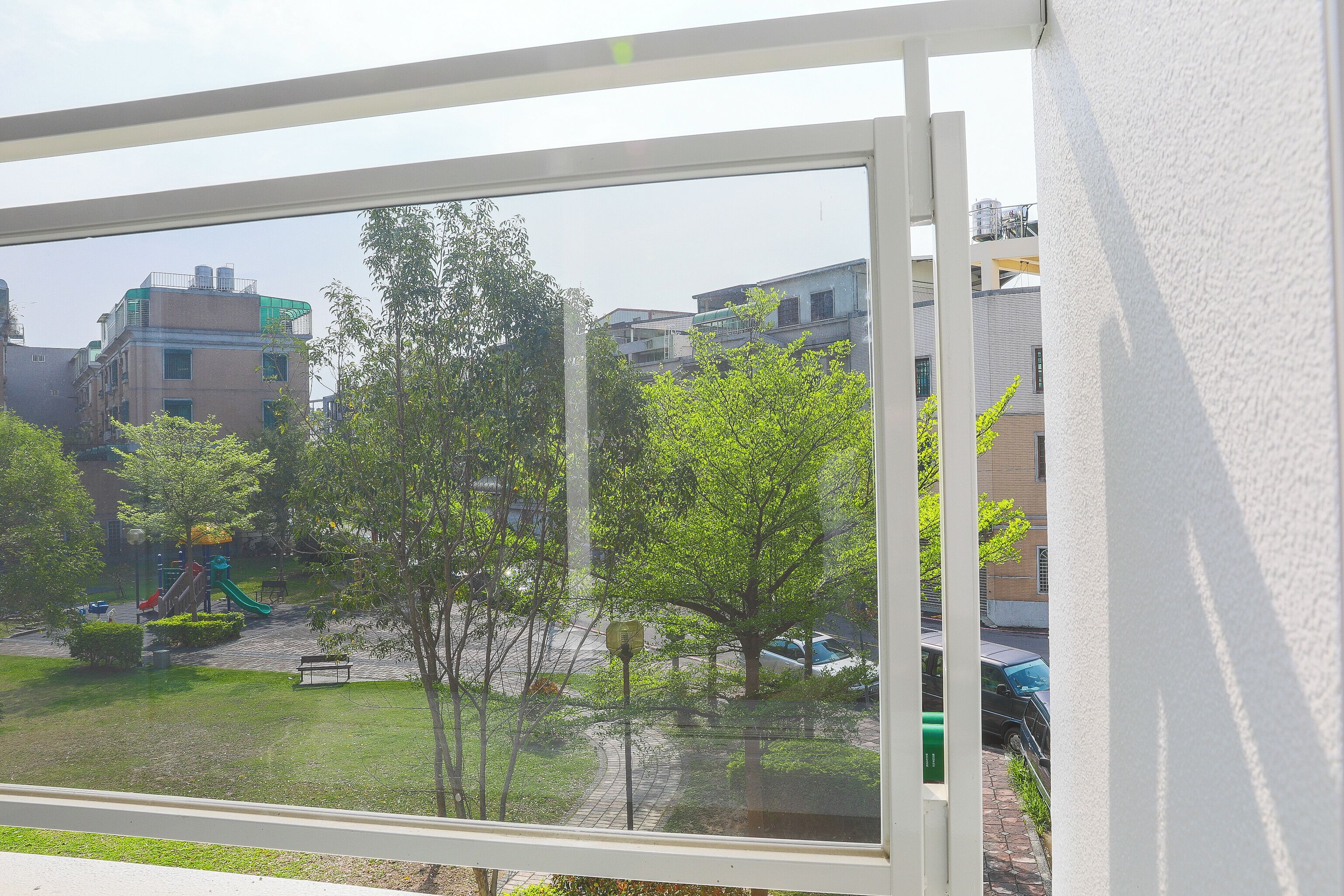 A view through a window of a residential area with a playground, trees, and buildings.