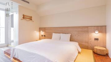 A modern hotel room with a large bed, wooden headboard, bedside lamps, and a small wooden stool.