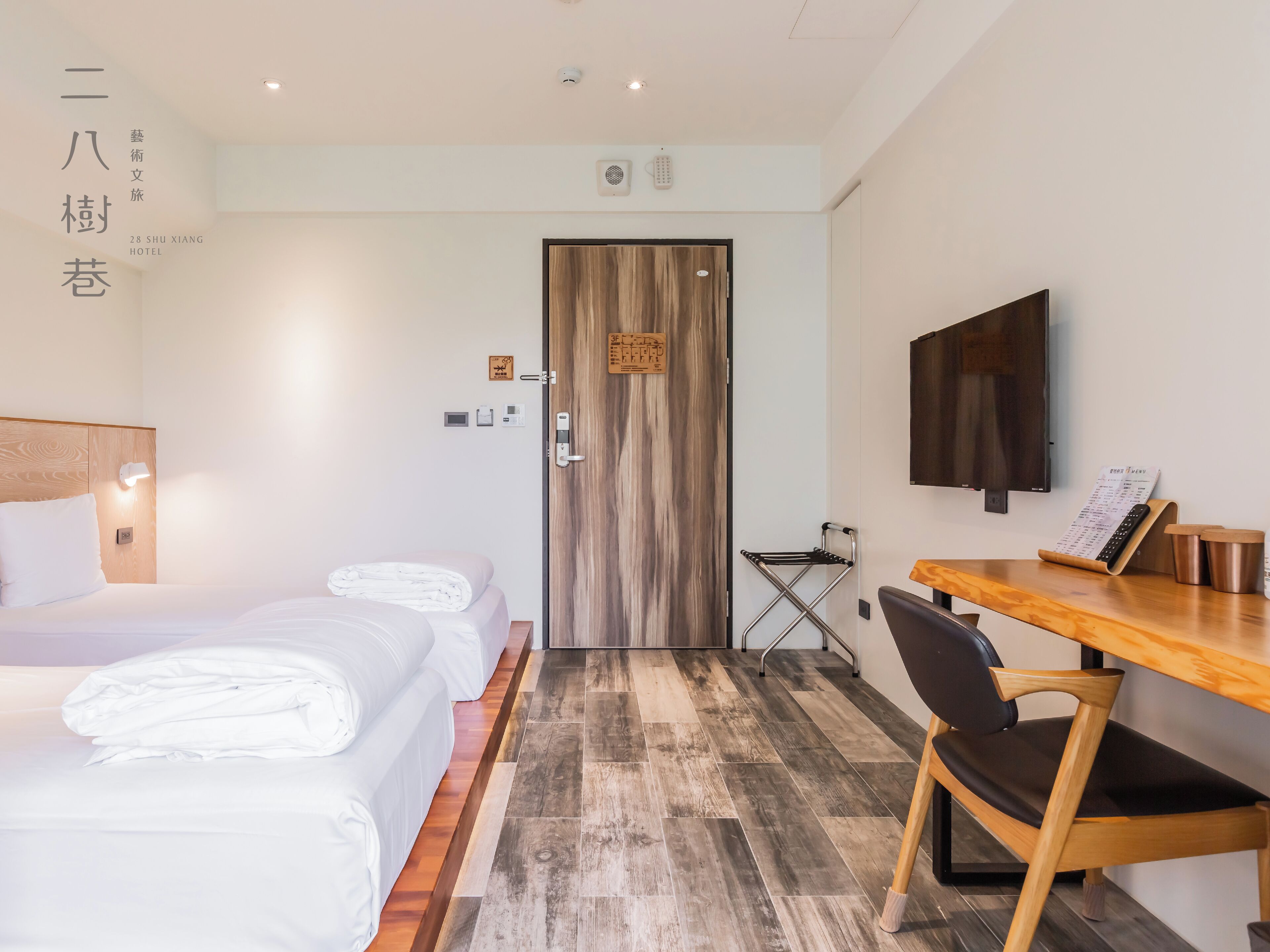 Une chambre d’hôtel avec un lit, un bureau, une chaise, une télévision et une porte en bois.