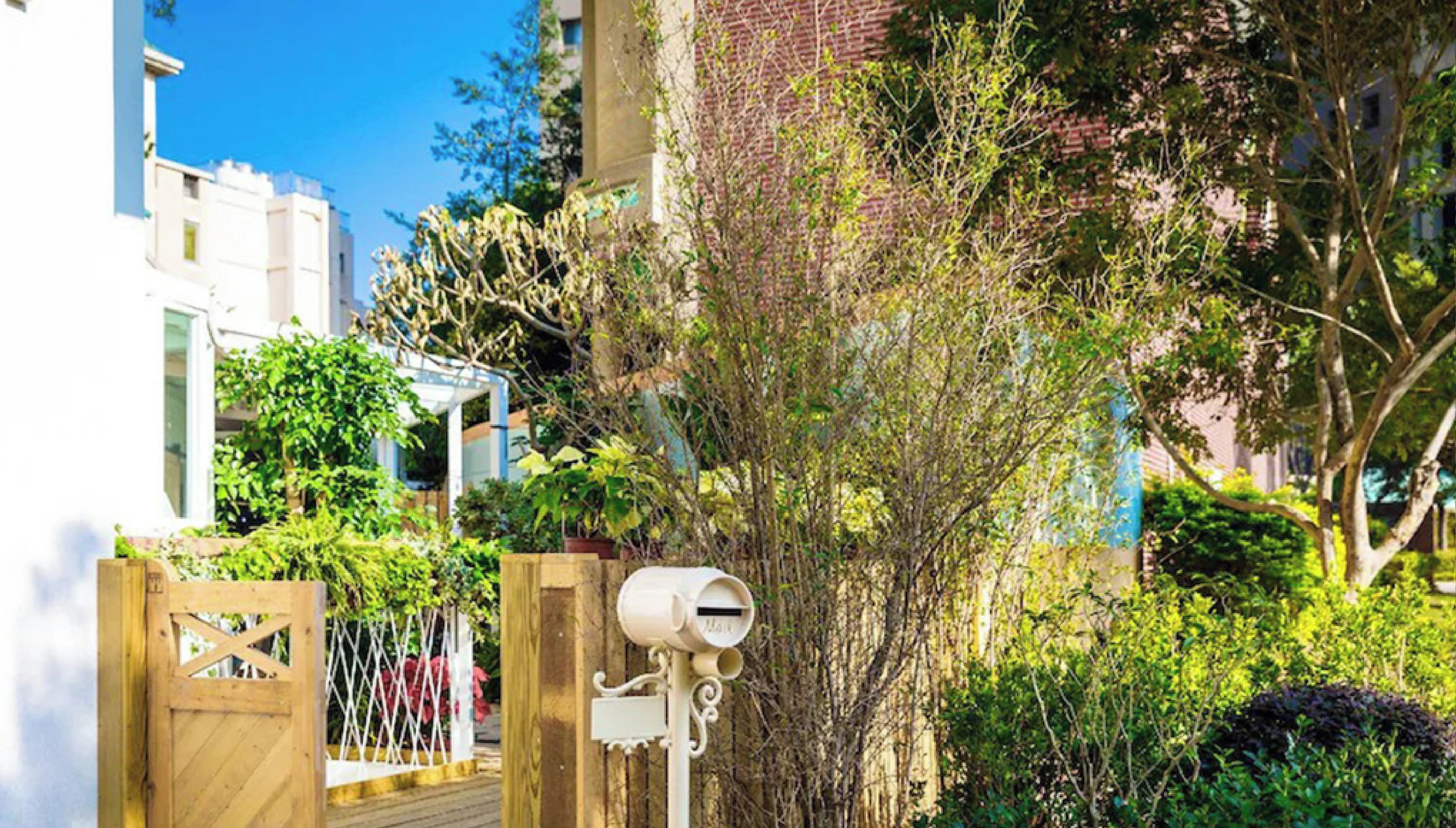 A gated entrance with a mailbox, lush greenery, and a building in the background.