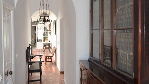 A hallway with a tiled floor, a wooden cabinet with glass doors, and a hanging light fixture. - In the center, apartment in manor house. (Sanlúcar de Barrameda)