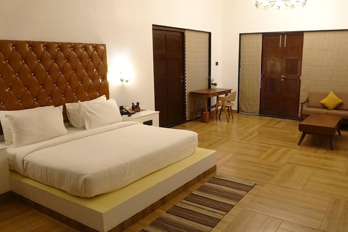A hotel room with a large bed, a desk, a sofa, and a chair.