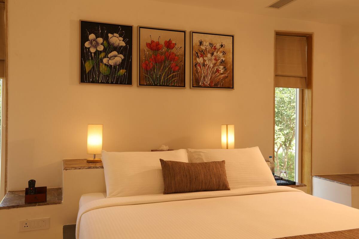 A hotel room with a large bed, two bedside lamps, and three framed floral paintings on the wall.