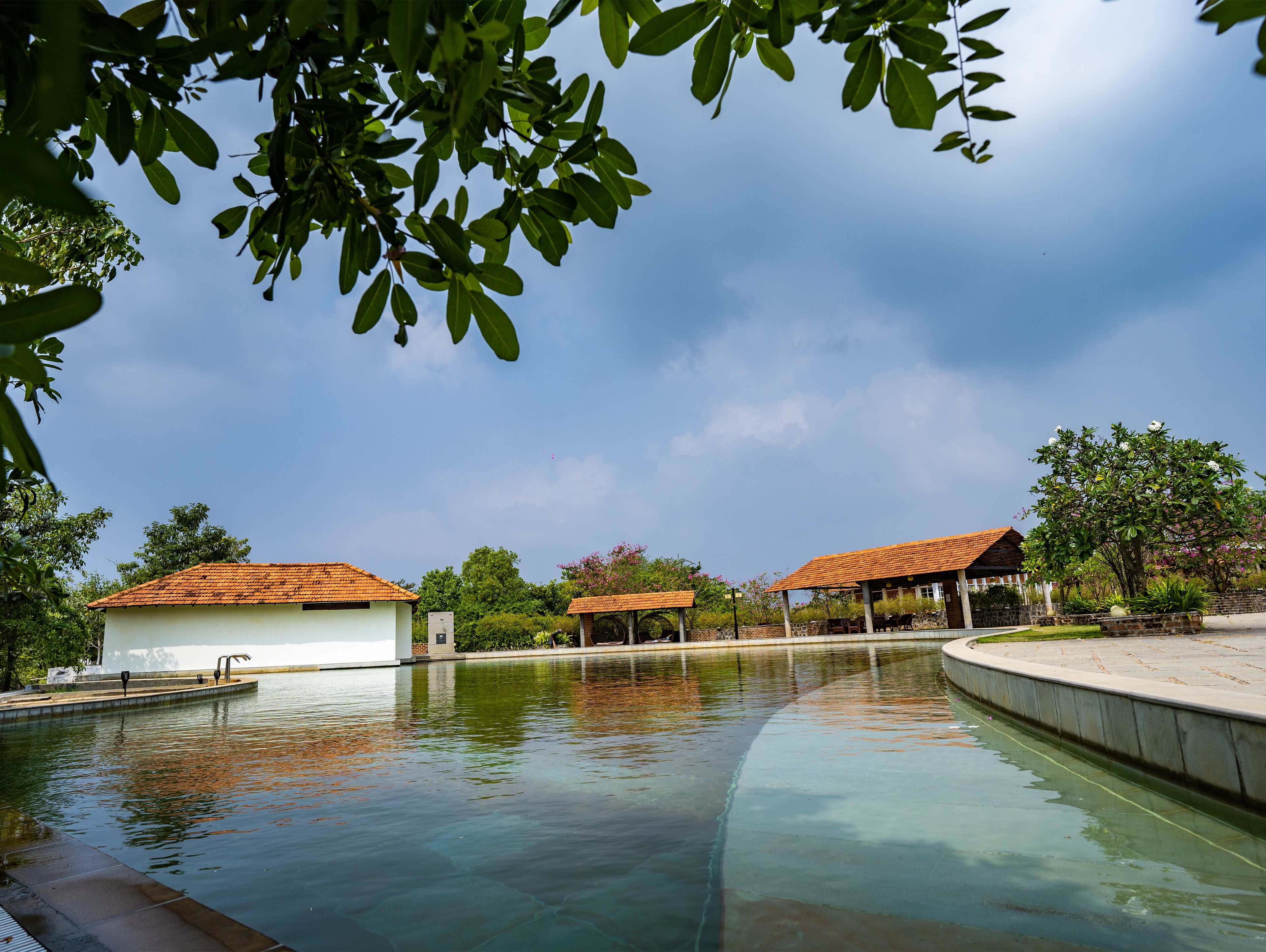 A swimming pool with a clear view of the sky, surrounded by buildings with red roofs and greenery.
