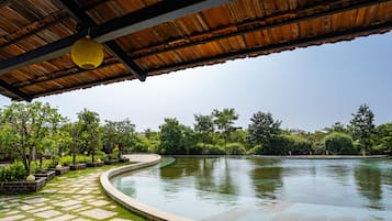 A covered outdoor area with a curved pool, stone pathway, and lush greenery.