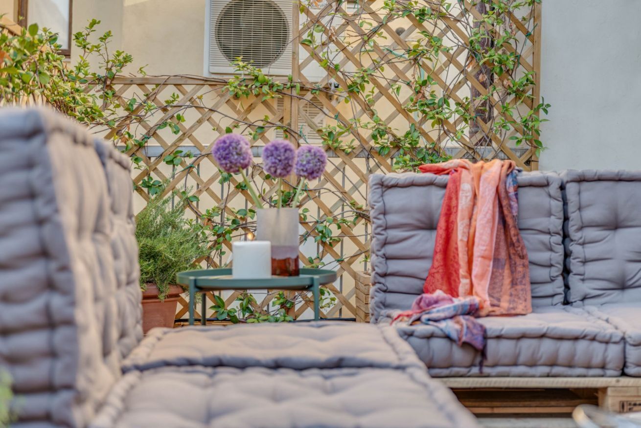 A cozy outdoor seating area with cushioned chairs, a small table with a candle, and a decorative plant arrangement.