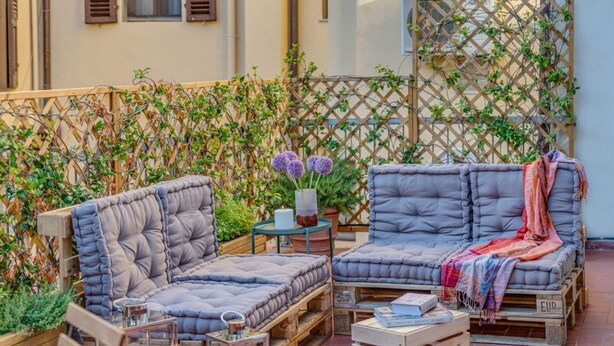 A cozy outdoor seating area with cushioned benches and a small table, surrounded by a wooden fence and potted plants. - Apartments Florence San Lorenzo Terrace (Firenze)