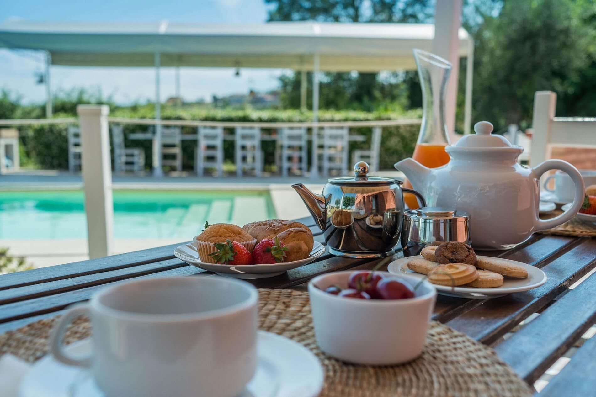 Un plateau de petit-déjeuner avec des viennoiseries, une théière et une tasse, placé près de la piscine.