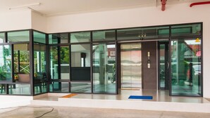 A modern building entrance with glass doors and windows, a concrete floor, and a visible outdoor area with greenery. - Innara Hotel (Pattaya)