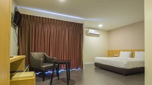 A hotel room with a bed, a desk with a chair, an air conditioning unit, and a curtain. - Innara Hotel (Pattaya)