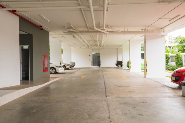 A covered parking area with two cars parked, white walls, and visible pipes on the ceiling.
